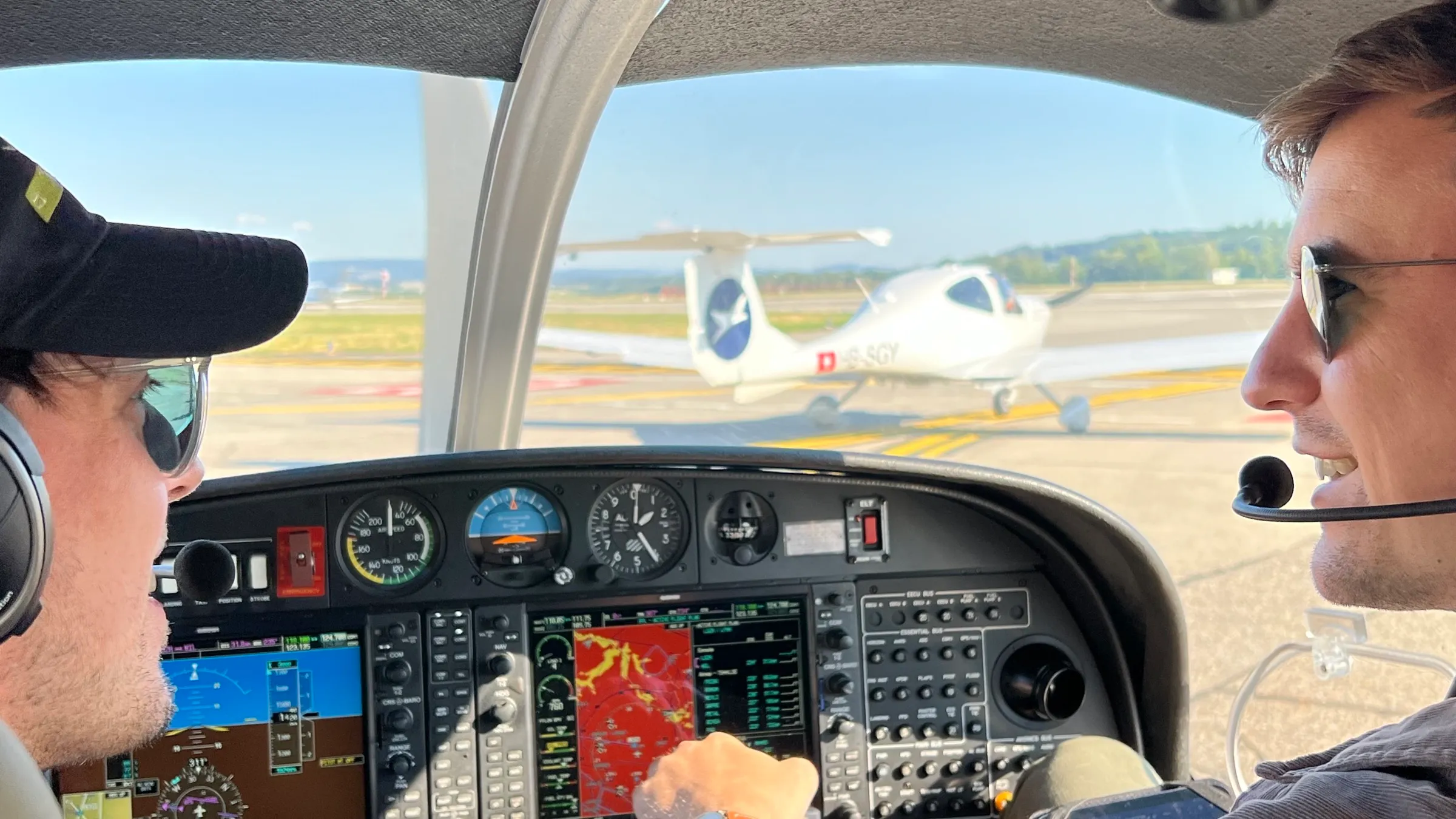 Two pilots in a Diamond DA40 cockpit with the second aircraft taxiing ahead at Zürich