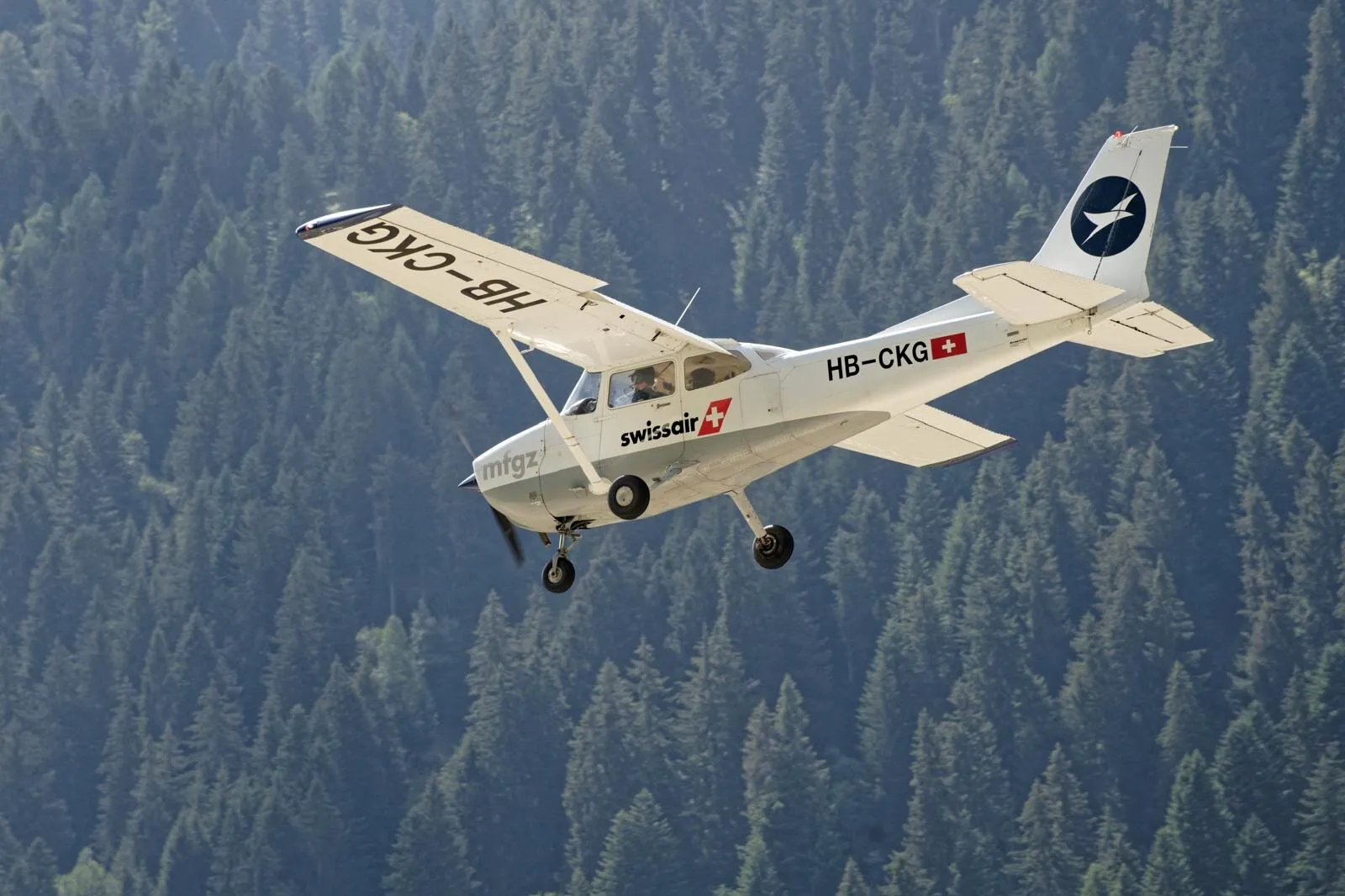 Cessna 172 HB-CKG in swissair livery on approach to Ambri over forested terrain